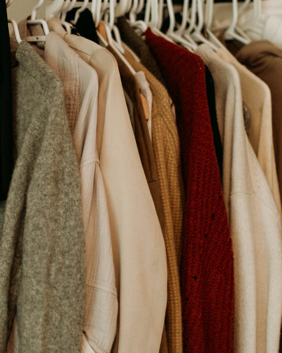 A rail of camel, cream and burgundy coats on wooden hangers