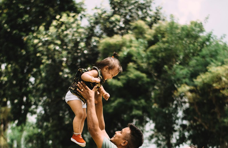 Father lifting his young daughter into the air in a park
