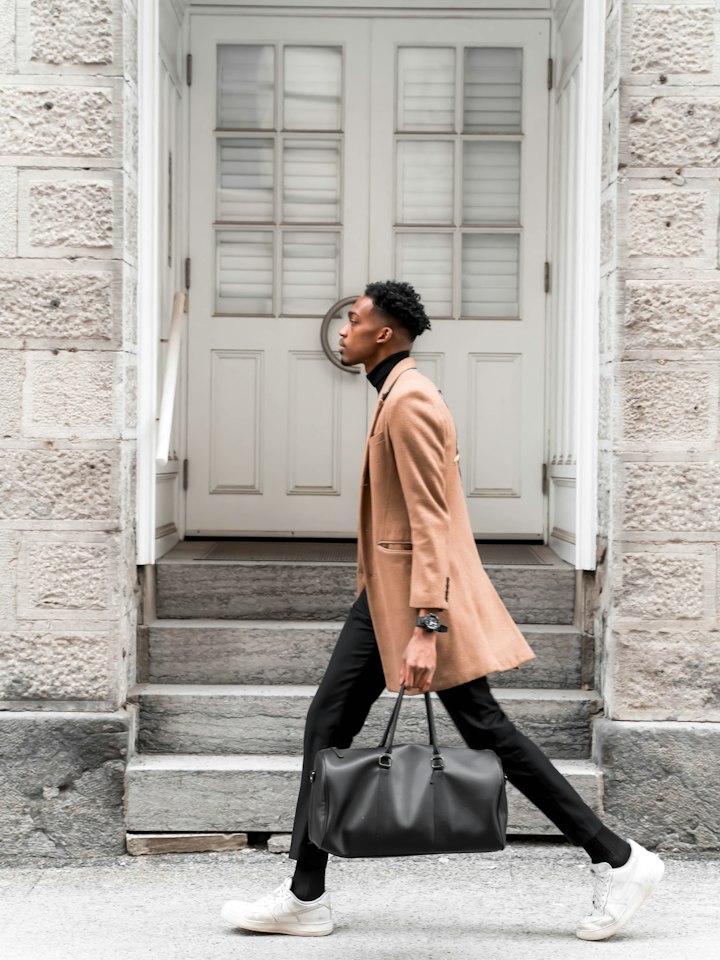 Man in a camel overcoat carrying a leather weekender bag