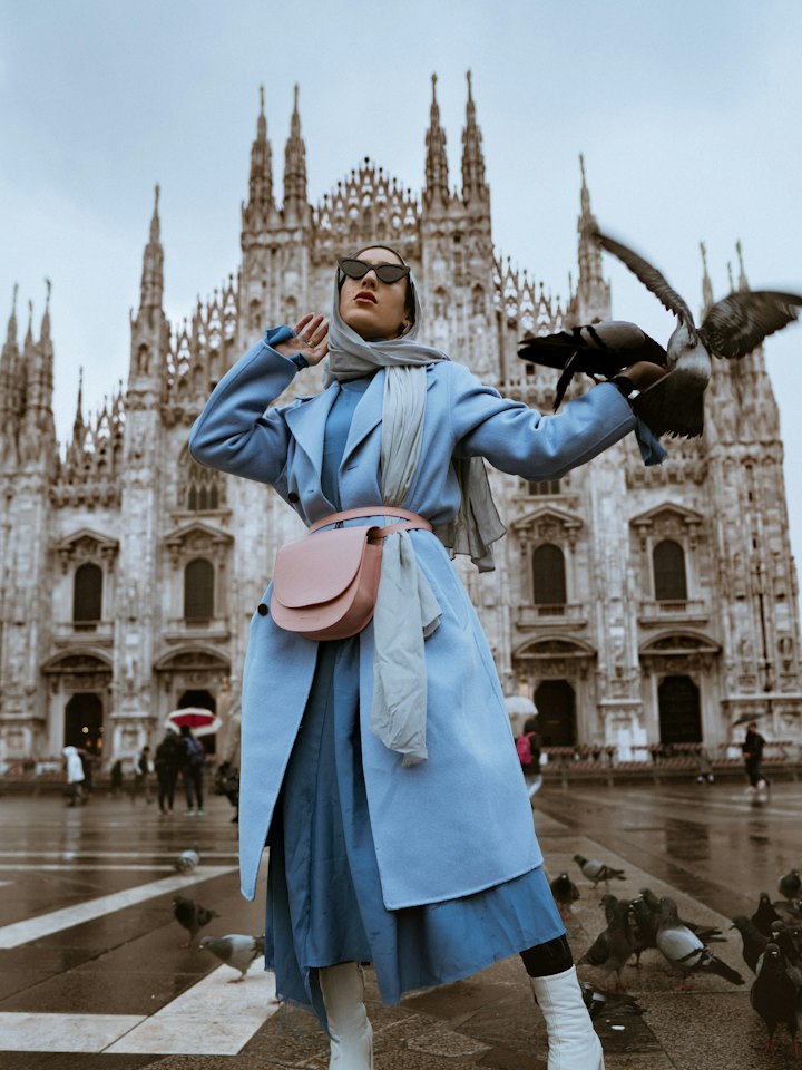 Woman in a pale blue coat and white boots in a city square